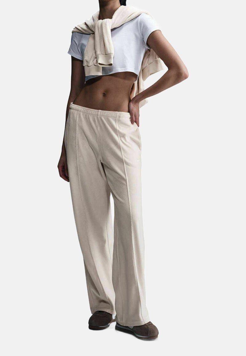 Beige wide-leg pants with a smooth texture, featuring stitched detailing. Paired with a fitted white crop top and a light sweater draped over the shoulders.