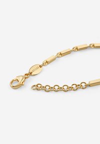 Bransoletka z ogniw prostokątnych w kolorze złotym, z zapięciem na homara i małą zawieszką z wygrawerowaną nazwą marki, o gładkim wykończeniu.