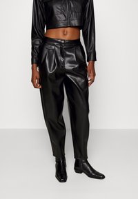 Zwarte faux leren cropped jack met lange mouwen, gecombineerd met hoogzittende zwarte faux leren broeken. Beide hebben een soepele textuur en een aangesloten ontwerp.