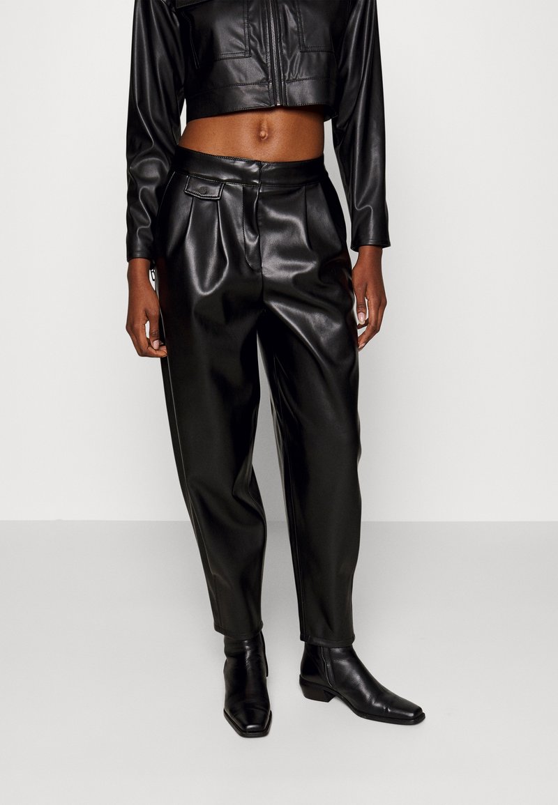 Zwarte faux leren cropped jack met lange mouwen, gecombineerd met hoogzittende zwarte faux leren broeken. Beide hebben een soepele textuur en een aangesloten ontwerp.
