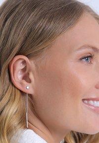 Boucles d'oreilles en argent avec un petit clou rond et une chaîne suspendue ornée d'une barre droite. Texture lisse, design épuré, style minimaliste.