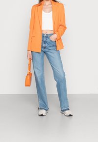 Blazer naranja, top corto blanco, jeans de talle alto azul claro y zapatillas beige. Los accesorios incluyen un pequeño bolso naranja.