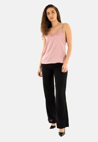 Camiseta de satén rosa con encaje, tirantes finos; combinada con pantalones de pierna ancha negros y tacones altos negros. Modelo de pie sobre un fondo neutro.