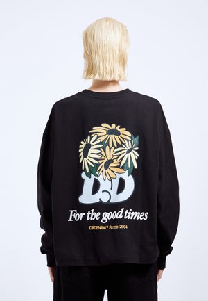 Felpa nera a maniche lunghe con una grande grafica floreale gialla e verde sul retro, accompagnata dal testo "Per i bei momenti" e "DD."