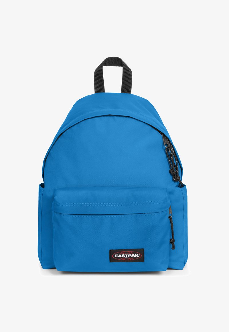 Sac à dos en tissu bleu de forme arrondie, avec une poche avant zippée et un patch logo noir. Dispose d'une poignée supérieure et de bretelles ajustables.