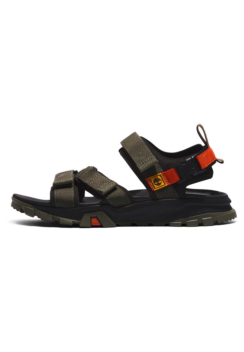 Dark green and black hiking sandals with adjustable straps, textured fabric, and a rugged sole featuring orange accents and a logo patch.