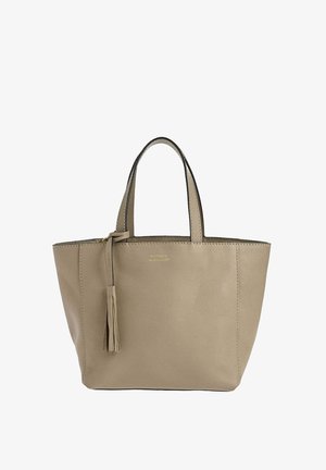 Sac à main en cuir beige avec deux poignées et un pompon en cuir assorti suspendu à l'une des poignées, structuré avec des détails de couture visibles.