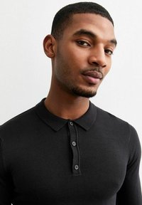 Zwarte poloshirt met lange mouwen van gebreide stof, met een kraag, een vijfknops sluiting en een getailleerd ontwerp. Soepele textuur over de hele lengte.