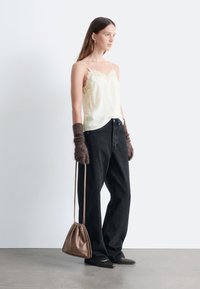 Seidene Camisole mit Spitze, dunkle lockere Jeans, braune gestrickte Handschuhe und eine glänzende braune Tasche. Schwarze spitze Schuhe runden das Outfit ab.
