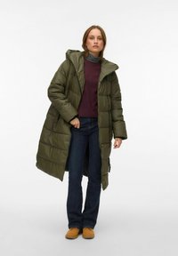 Olive roheline kapuutsiga polsterdatud mantel, millel on tõmblukuga sulgemine ja küljetaskud, kantud üle marooni kampsuni ja siniste teksade.