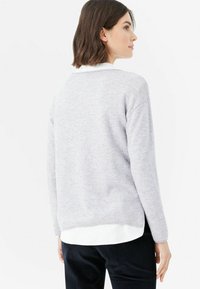 Grau Sweatshirt mit lässiger Passform, weichem Material und gerippten Bündchen. Übereinander getragen mit einem weißen Hemd, kombiniert mit dunklen Baumwollcordhosen.