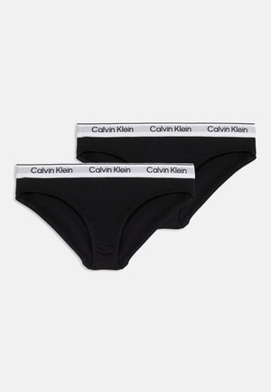 To sorte lavtaljede bikini-trusser med hvide elastiske linninger med gentagne "Calvin Klein" logoer på en lys baggrund.