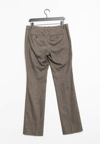 Bruine op maat gemaakte broeken hangen aan een zwarte hanger, met de achterkant zichtbaar met knoopzakken en riemlussen.