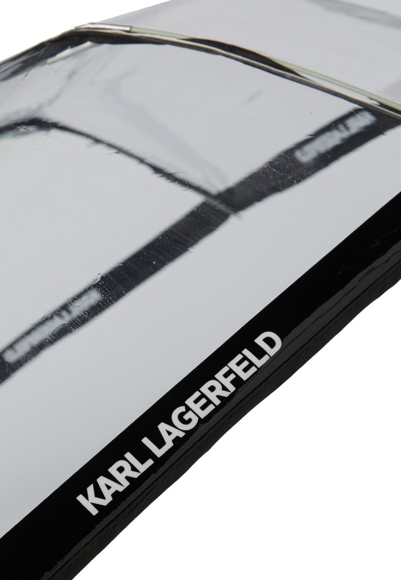 Una bustina lucida, argentata con un bordo nero, contrassegnata con la scritta "KARL LAGERFELD". La superficie è liscia e i cablaggi sono visibili lungo la parte superiore.