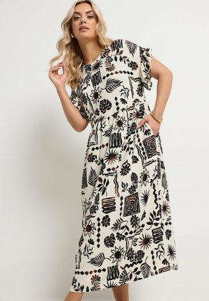 Frau posiert in einem weißen Midikleid mit schwarzen und braunen abstrakten floralen und geometrischen Mustern, mit Rüschenärmeln und Taschen.