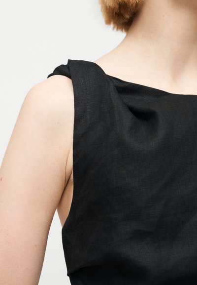 Μαύρο φόρεμα με δομημένο, draped ντεκολτέ και παχύ ιμάντα. Το ύφασμα έχει υφή που προσθέτει οπτικό ενδιαφέρον.