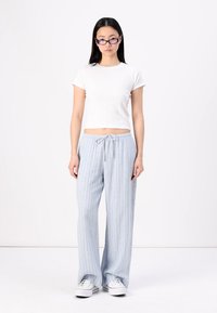 Top court à manches courtes blanc associé à un pantalon large rayé bleu clair. Il possède une taille élastique et un lien de serrage. Baskets incluses.