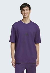 Μωβ κοντομάνικο μπλουζάκι με στρογγυλή λαιμόκοψη και μικρό μαύρο λογότυπο Adidas στο στήθος. Μαλακό, αναπνεύσιμο ύφασμα με άνετη εφαρμογή.