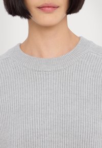 Pulover moale gri, cu dungi, cu gât rotund. Textura este tricotată cu dungi verticale, având o strălucire subtilă și fără embellishments vizibile.