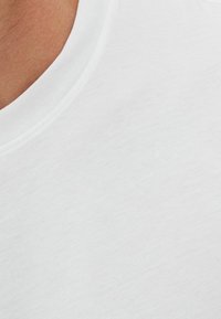 Biały bawełniany T-shirt z okrągłym dekoltem, z gładkiego, teksturowanego materiału o minimalistycznym wzornictwie, prezentujący czysty, neutralny kolor.