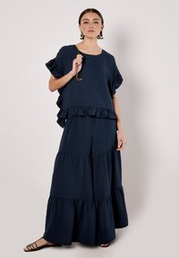 Navy blue layered dress with ruffle accents and short sleeves. Soft fabric with a flowy design, featuring a tiered skirt.
