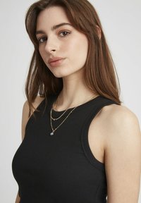 Débardeur noir à côtes avec une coupe ajustée. Présente des colliers en or superposés, dont un avec un charme bleu, et une texture lisse sur le tissu.