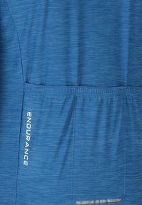 Tissu bleu avec une poche arrière horizontale et le mot "ENDURANCE" imprimé verticalement sur le côté gauche de la poche.