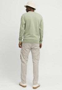 Lys grønn crewneck-genser, beige cargobukser med sidelommer og beige bøttehatt. Myk tekstur, avslappet passform, nøytralt fargepalett.