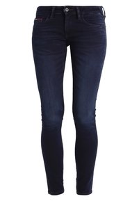 Tajta jeans i mörkblå denim med fem fickor. Inkluderar en subtil röd accent nära fickan och silverfärgad knapplåsning.