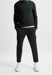 Mörkgrön texturerad stickad tröja, vit crew-neck tröja under, ihop med avsmalnande svarta byxor och vita sneakers.