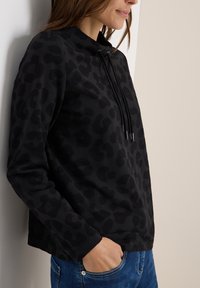 Sweatshirt noir avec un motif léopard subtil, doté d'un col haut, de cordons de serrage et d'un tissu texturé. Il a des manches longues et une coupe décontractée.