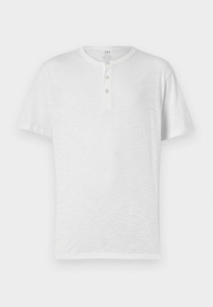 Valkoinen lyhythihainen henley-paita, jossa on kolme nappia, valmistettu kevyestä ja hieman teksturoidusta kankaasta. Pyöreä kaula-aukko, rento istuvuus.