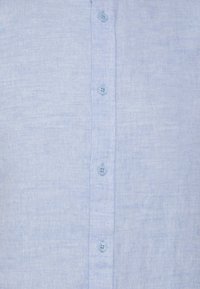 Camicia di lino azzurro chiaro con bottoni sul davanti, sei bottoni coordinati, una sottile trama e colletto classico.