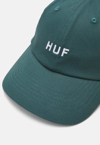 Zöld pamut sapka fehér hímzett "HUF" logóval, ívelt silddel és látható varrási részletekkel. Hat szellőzőlyukkal rendelkezik.