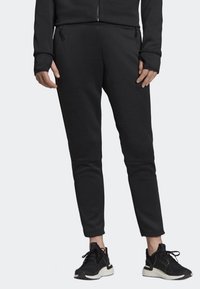 Svarta joggingbyxor med smal passform, med diskreta knäpaneler och fickor med dragkedja. Matchas med svarta löparskor.