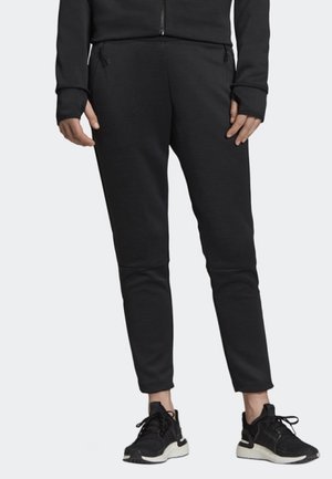 Pantalons de jogging noirs à coupe ajustée, dotés de panneaux au niveau des genoux et de poches zippées. Associés à des chaussures de sport noires.
