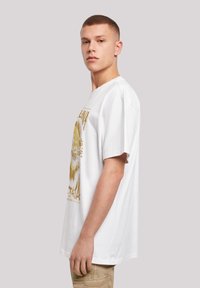 White cotton t-shirt with short sleeves and a loose fit, featuring a gold printed graphic design. The shirt has a round neckline.