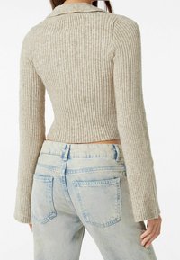 Geribbelde, beige cropped trui met een kraag en lange mouwen, gecombineerd met lichtblauwe, vervaagde high-waisted jeans met achterzakken.