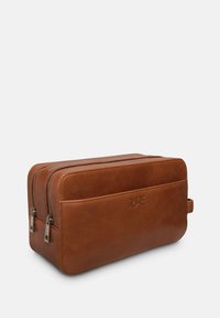 Braune Leder-Doppeltasche mit zwei Reißverschlussfächern und einem seitlichen Griff, auf der Vorderseite mit dem Wort "PURE" geprägt.