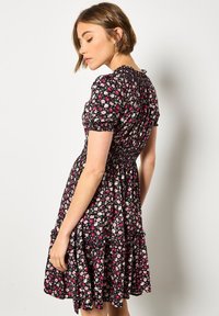 Mustat kukkakuosiset mekko, jossa on lyhyet puffihihat, rypistetty yläosa ja kerroksellinen hame; mukana pieniä vaaleanpunaisia ja valkoisia kukkia kauttaaltaan.