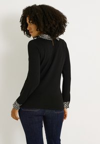 Top negro de manga larga con cuello y puños de estampado de leopardo, con una abertura en forma de ojal en la parte de atrás. Combinado con unos vaqueros azul oscuro.