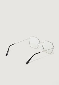 Hõbedased piirilised kuue nurga prillid, milles on selged läätsed ja mustad tipud templites. Kujundatud minimalistlikult, kergetest metallmaterjalidest ja peente detailidega.