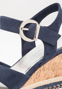 Sandale compensée en daim bleu marine avec boucle ronde argentée et semelle en liège avec détails texturés bleu et fibres naturelles.