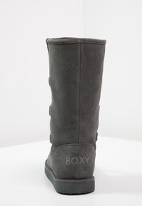 Botte en suede grise, haute jusqu'au genou, avec une surface texturée, dotée d'une semelle en caoutchouc plate et d'un logo de marque à l'arrière. Aucune quincaillerie ou accent visible.