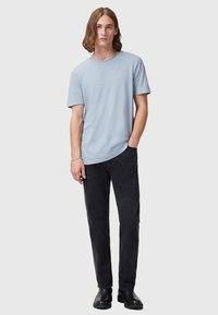 T-shirt di cotone azzurro chiaro con maniche corte, scollo rotondo e orlo curvo, abbinato a pantaloni di denim neri e stivali neri.
