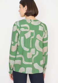Zielona bluzka z abstrakcyjnym wzorem beżowych pociągnięć pędzla, długimi rękawami, zapinanymi mankietami i luźnym krojem z okrągłym dekoltem.