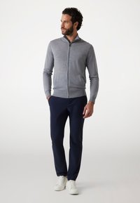 Maglione grigio con zip e colletto alto, abbinato a pantaloni blu e sneakers bianche; texture morbida e design slim-fit.