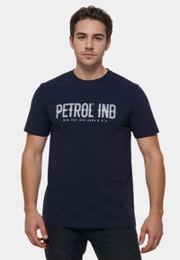 Marineblauw katoenen T-shirt met korte mouwen, voorzien van een gedurfde witte opdruk met de tekst "PETROL IND" op de borst. Soepele textuur, ronde hals.