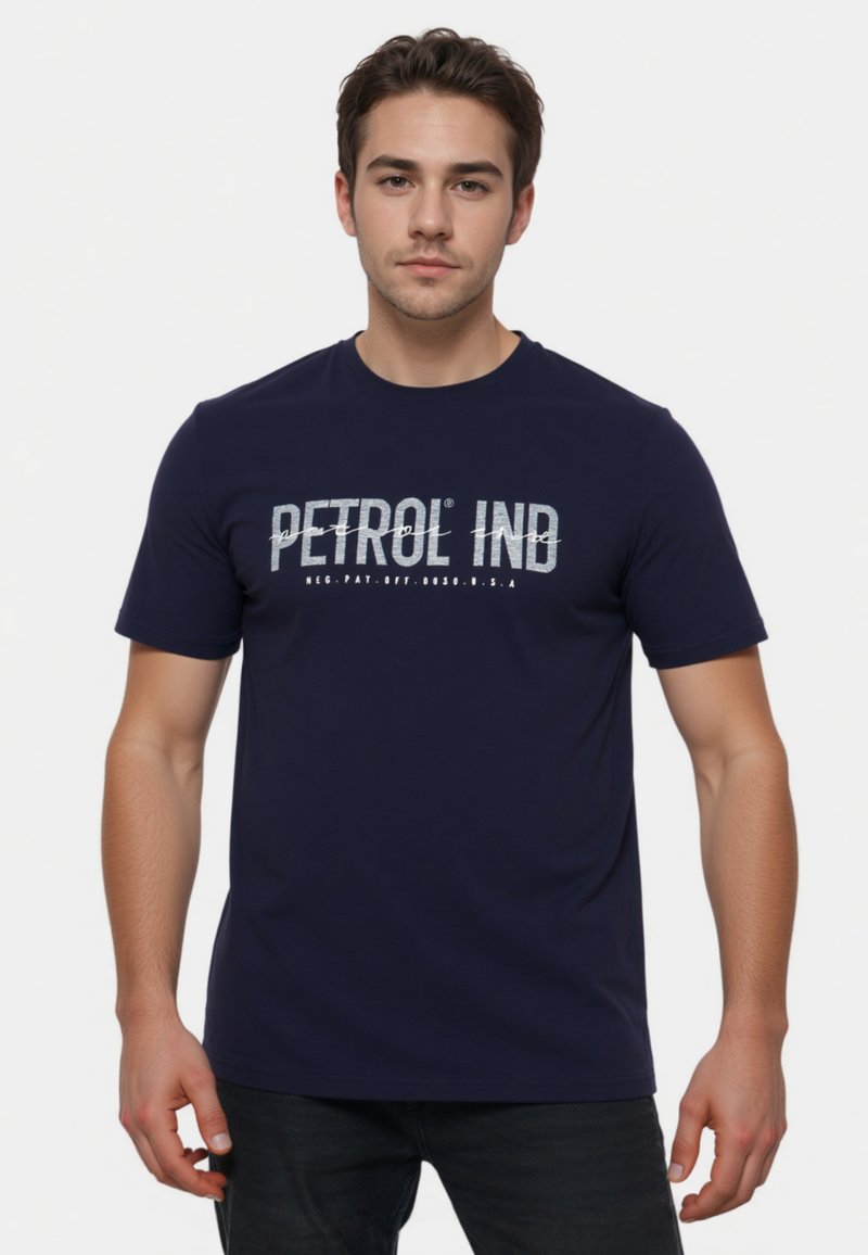 Marineblauw katoenen T-shirt met korte mouwen, voorzien van een gedurfde witte opdruk met de tekst "PETROL IND" op de borst. Soepele textuur, ronde hals.