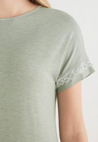 Top verde de manga corta hecho de una tela suave, con detalles de encaje en las mangas, cuello redondeado y textura suave.